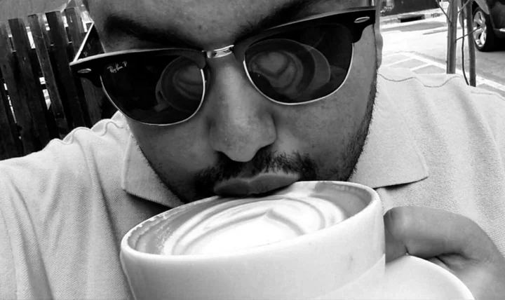 Daniel Molinares, who founded Molex Coffee, in sunglasses at an outdoor table, lifting a wide cup of cappuccino with latte art to his mouth