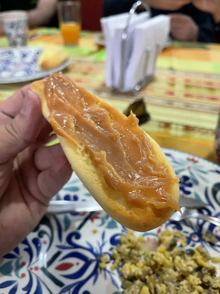 A split bread roll spread thickly with arequipe, held over a painted ceramic plate