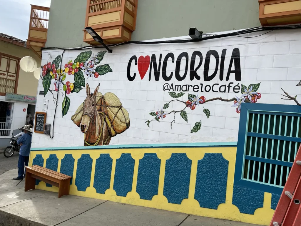 A mural on a Concordia street wall spelling out the town name beside a painted coffee picker and a drum
