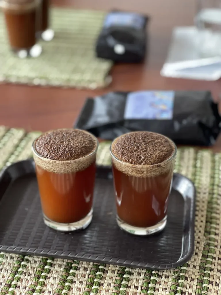 Two glasses of coffee at the cupping table with a thick crust of soaked grounds risen to the top