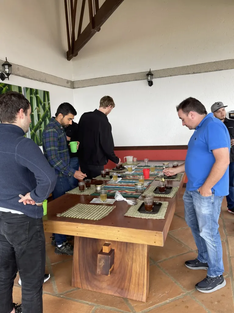 People leaning over a long wooden table set with rows of cupping glasses, spoons and score sheets