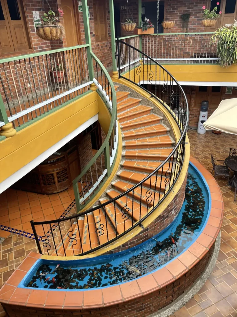 A curved wooden staircase winding down into a tiled hacienda courtyard planted with ferns