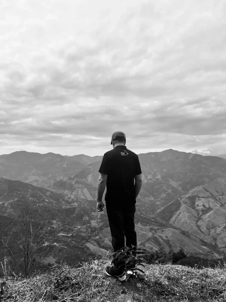Black and white photograph of a figure standing alone on a ridge looking out over layered mountains